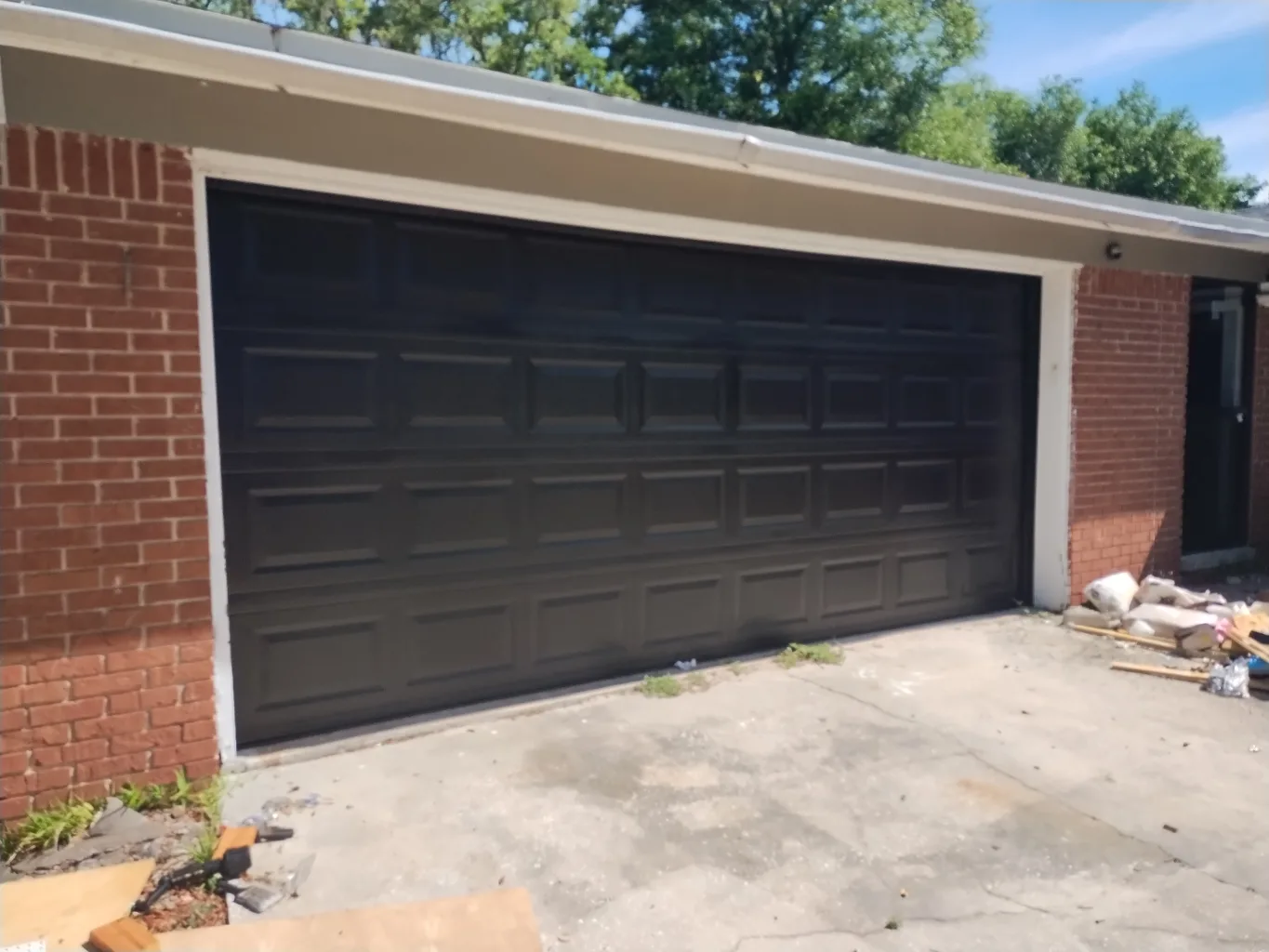 A garage door technician working on a residential door replacement job — mid-task, hands, tools and the work itself in sharp focus, the rest of the space softly out of focus